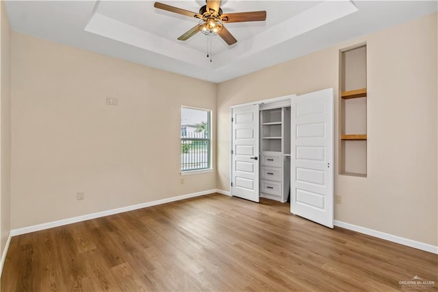 unfurnished bedroom featuring a tray ceiling, ceiling fan, a closet, and wood-type flooring