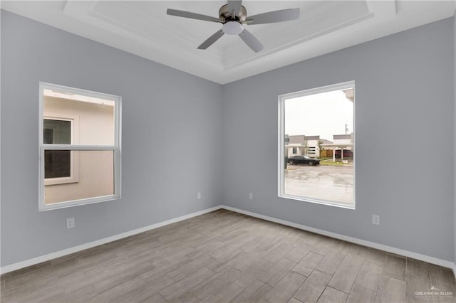 spare room featuring baseboards, ceiling fan, a tray ceiling, and light wood-style floors