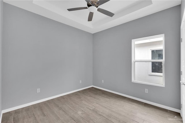 spare room with a ceiling fan, a raised ceiling, light wood-style flooring, and baseboards