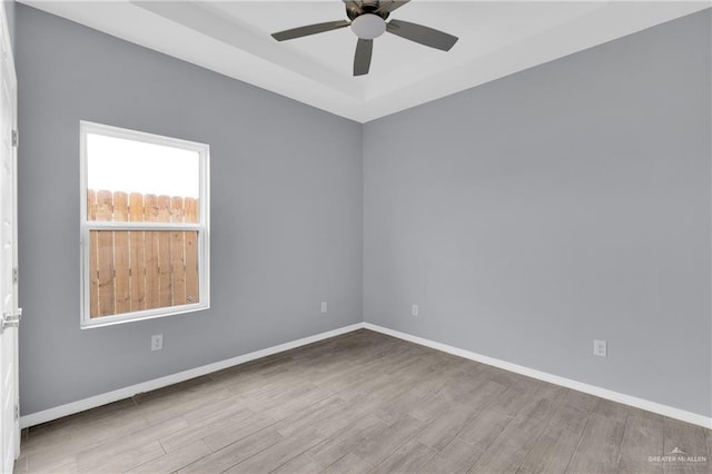 unfurnished room with light wood-style floors, a raised ceiling, baseboards, and a ceiling fan