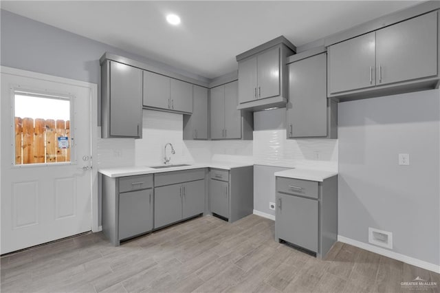 kitchen with light countertops, backsplash, a sink, and gray cabinetry