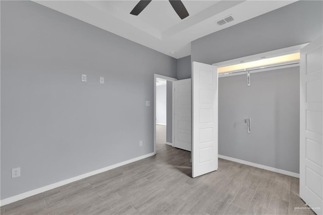 unfurnished bedroom featuring visible vents, a raised ceiling, baseboards, ceiling fan, and light wood-style flooring