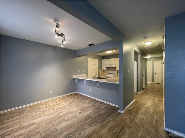 kitchen with visible vents, under cabinet range hood, wood finished floors, white electric range oven, and a peninsula