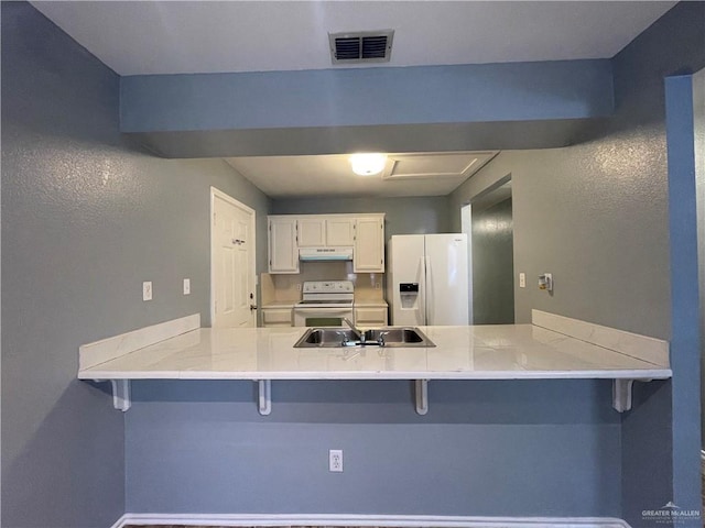 kitchen with under cabinet range hood, visible vents, white appliances, and a peninsula