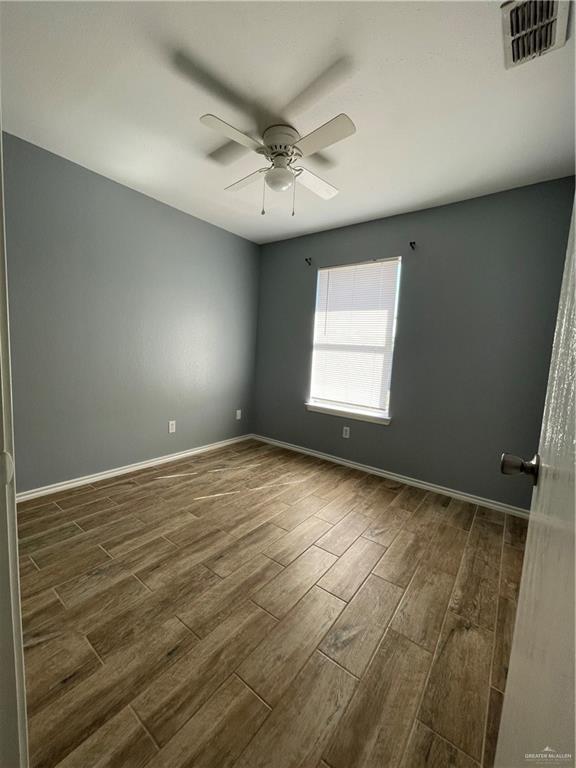 empty room featuring visible vents, baseboards, dark wood-type flooring, and ceiling fan