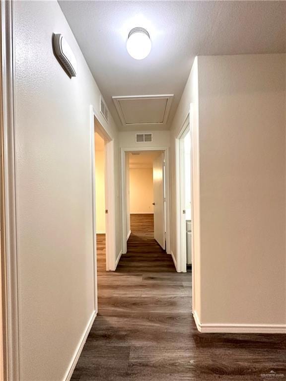 hallway featuring dark wood-style flooring, visible vents, and baseboards