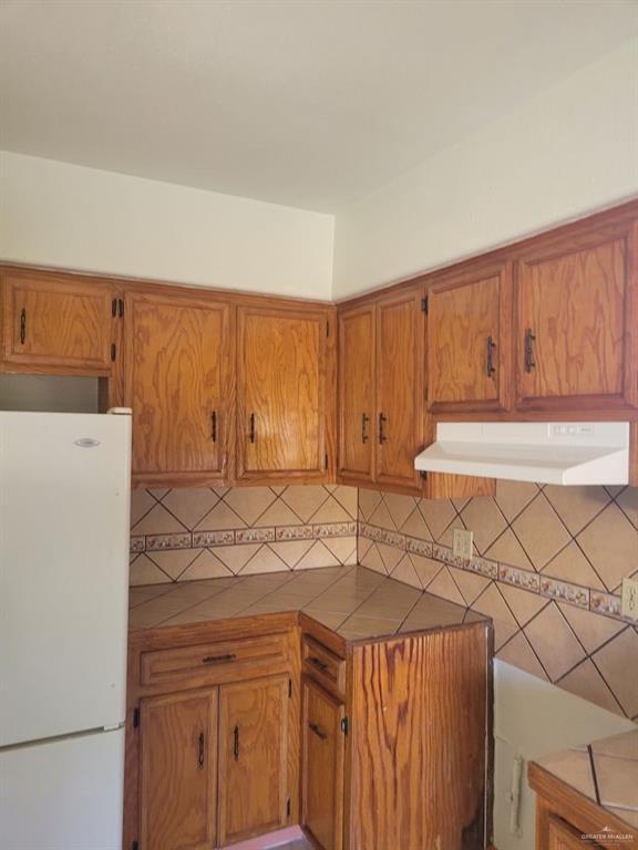233 W 4th St, La Joya, TX 78560 - kitchen with freestanding refrigerator, under cabinet range hood, brown cabinetry, and tile counters