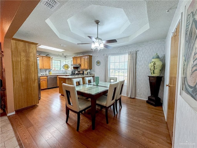 dining space with light wood-type flooring, a textured ceiling, a ceiling fan, and visible vents