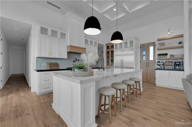 kitchen with an island with sink, pendant lighting, decorative backsplash, white cabinets, and light wood-type flooring