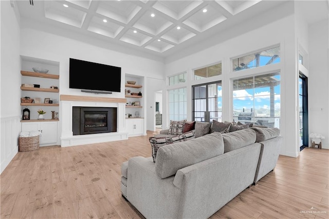 living room with beam ceiling, coffered ceiling, a high ceiling, built in features, and light hardwood / wood-style floors