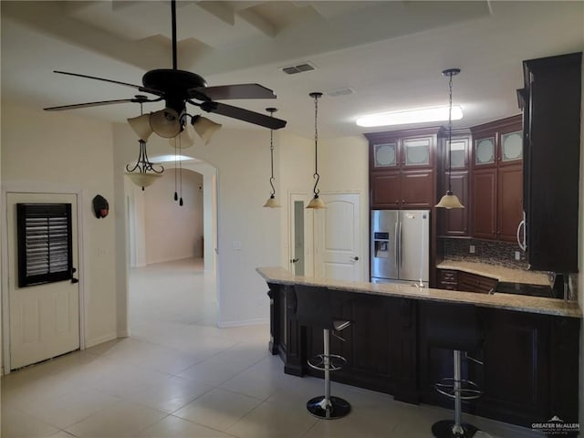 kitchen with stainless steel refrigerator with ice dispenser, a breakfast bar area, hanging light fixtures, and backsplash