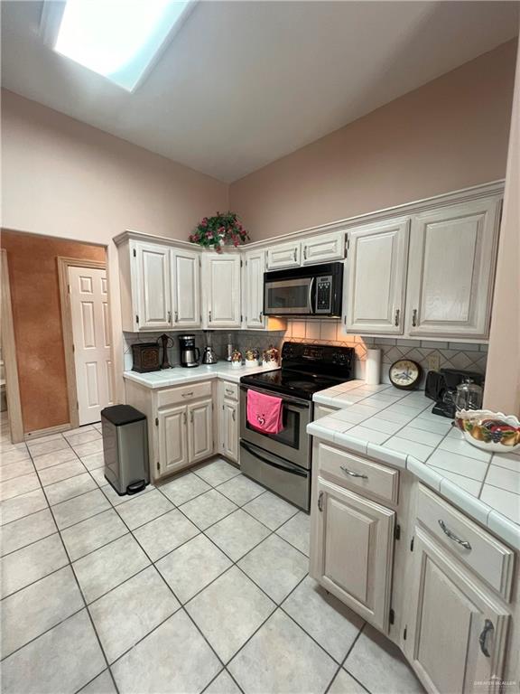 kitchen featuring tile countertops, white cabinetry, black electric range oven, and a skylight