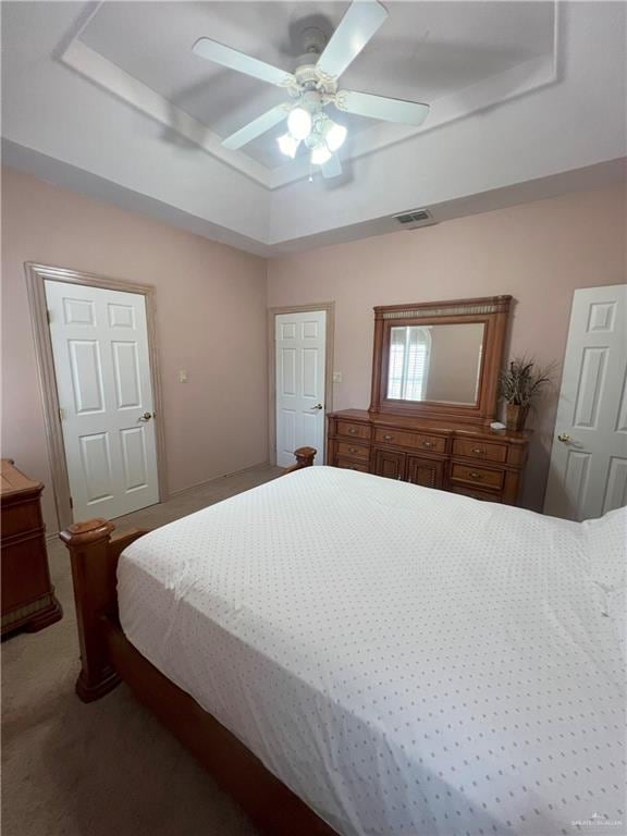 carpeted bedroom with a raised ceiling and ceiling fan