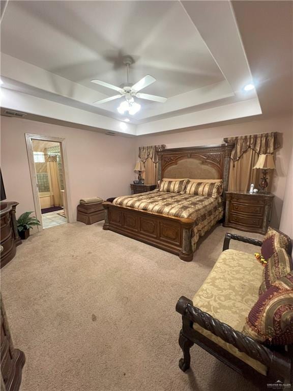 bedroom with ceiling fan, a raised ceiling, light colored carpet, and connected bathroom