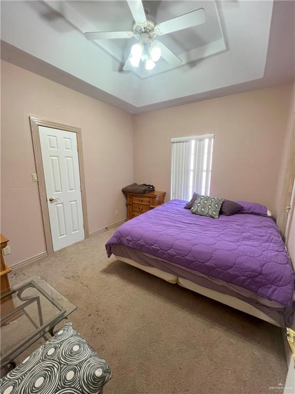 carpeted bedroom featuring ceiling fan and a raised ceiling