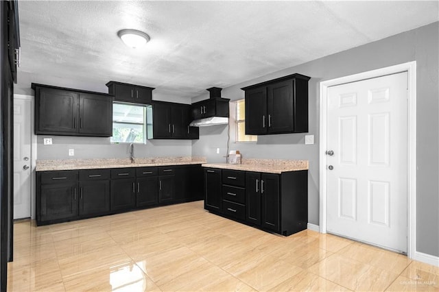 3109 Raul Gonzalez Dr, Mercedes, TX 78570 - kitchen featuring dark cabinets, under cabinet range hood, a textured ceiling, and light stone countertops