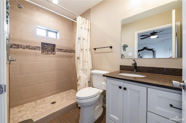 full bathroom featuring toilet, a ceiling fan, tiled shower, and vanity