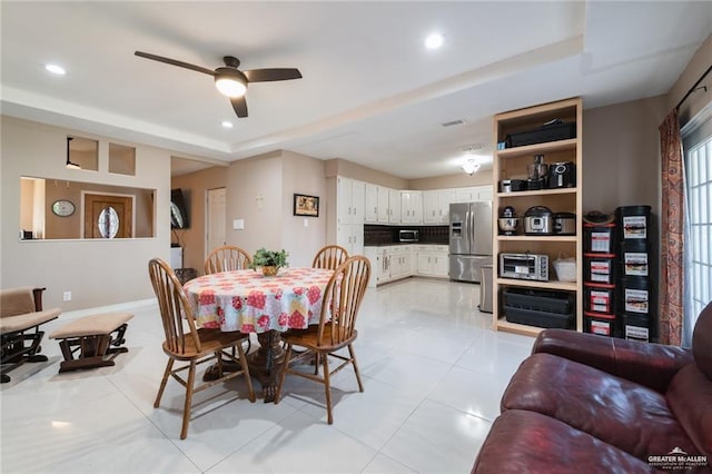 dining area with light tile patterned flooring, ceiling fan, and a tray ceiling