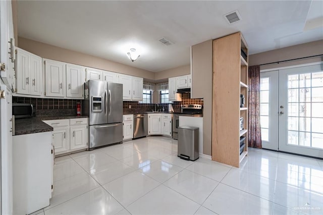 kitchen with white cabinets, appliances with stainless steel finishes, dark countertops, visible vents, and backsplash