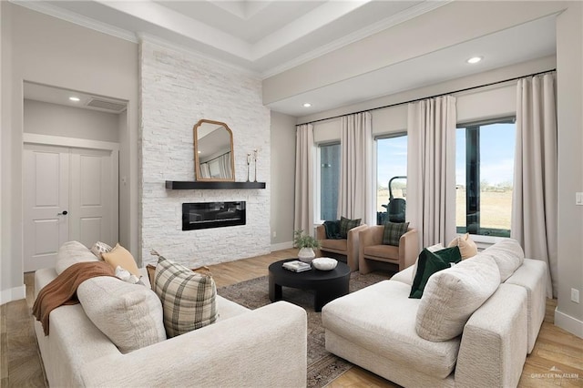 living room featuring crown molding, a stone fireplace, and light hardwood / wood-style floors