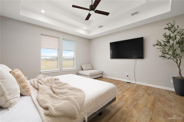 bedroom featuring ceiling fan, hardwood / wood-style floors, and a raised ceiling