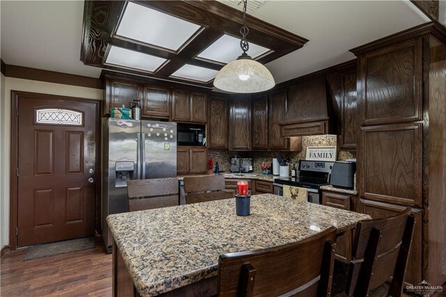 kitchen featuring light stone countertops, a kitchen island, decorative light fixtures, and appliances with stainless steel finishes