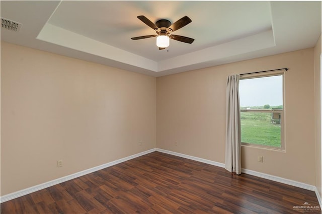 unfurnished room featuring dark hardwood / wood-style flooring, a tray ceiling, and ceiling fan