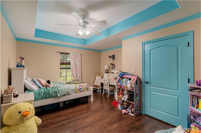 bedroom with dark hardwood / wood-style flooring, a tray ceiling, and ceiling fan