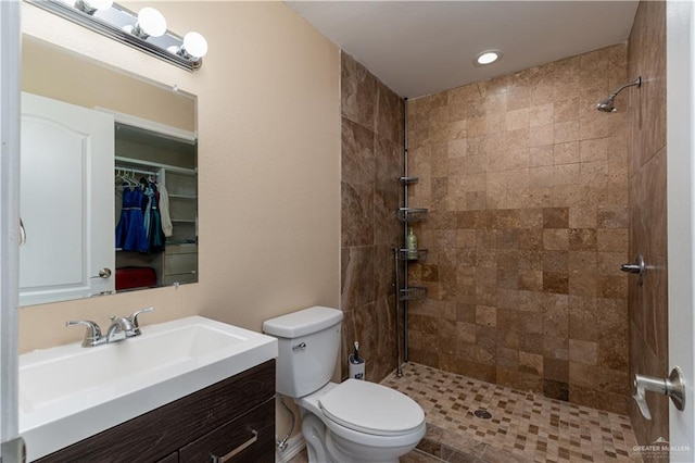 bathroom with toilet, a tile shower, and vanity