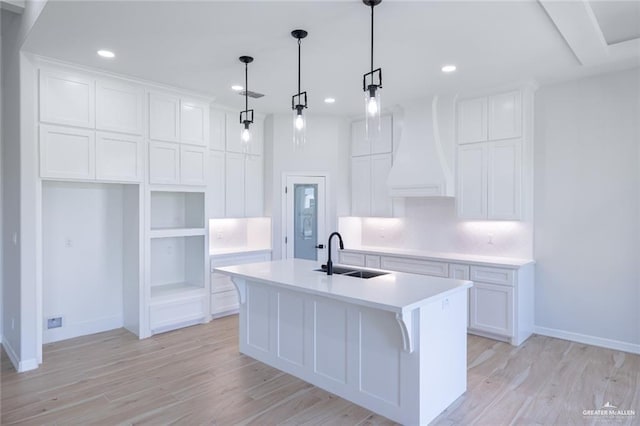 kitchen featuring sink, decorative light fixtures, a center island with sink, white cabinets, and custom exhaust hood