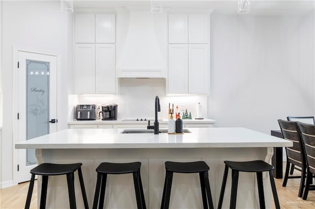 kitchen with a center island with sink, a kitchen breakfast bar, light wood-type flooring, and white cabinetry