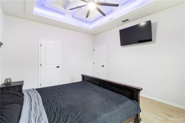 bedroom with ceiling fan, a raised ceiling, and light wood-type flooring