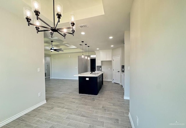 kitchen featuring coffered ceiling, ceiling fan with notable chandelier, a center island with sink, light hardwood / wood-style flooring, and white cabinets