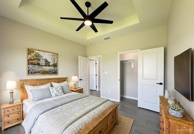 bedroom with a spacious closet, ceiling fan, dark hardwood / wood-style flooring, a tray ceiling, and a closet