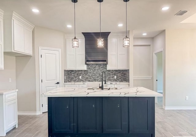 kitchen featuring pendant lighting, light stone countertops, white cabinetry, and an island with sink