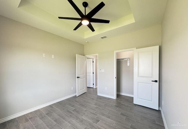 unfurnished bedroom with a walk in closet, a tray ceiling, ceiling fan, hardwood / wood-style floors, and a closet