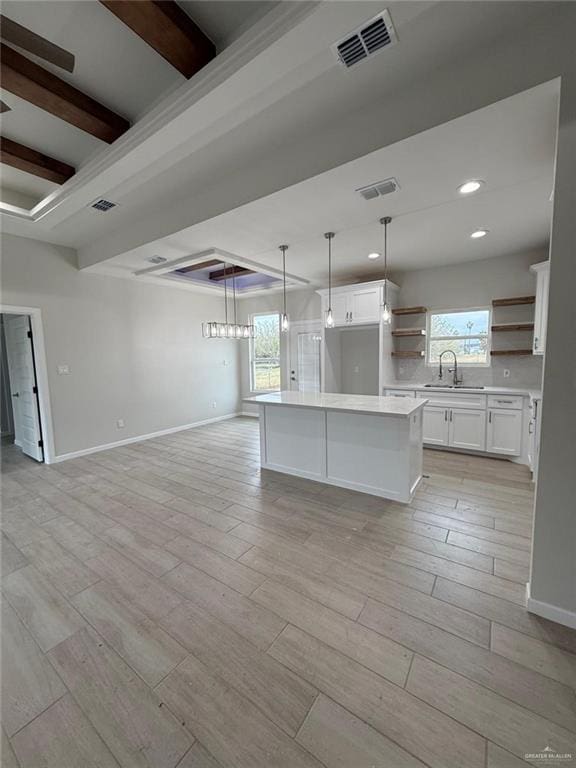 kitchen featuring white cabinetry, beam ceiling, a center island, and sink