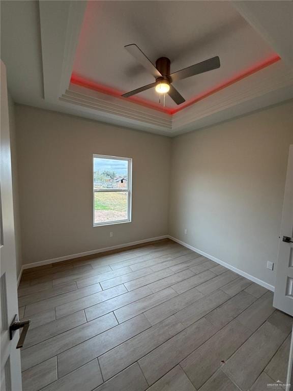 empty room with light hardwood / wood-style flooring, a raised ceiling, and ceiling fan