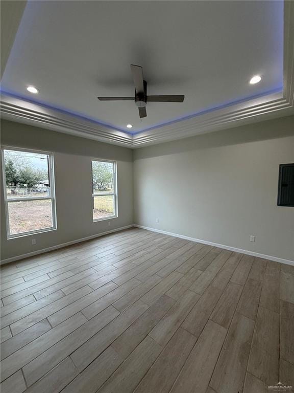 empty room featuring crown molding, ceiling fan, a tray ceiling, and light wood-type flooring