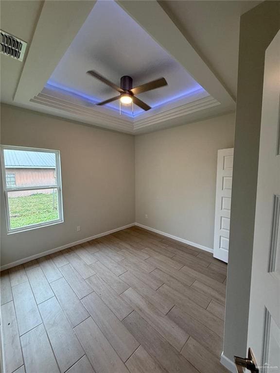 spare room with ceiling fan, a tray ceiling, and light wood-type flooring