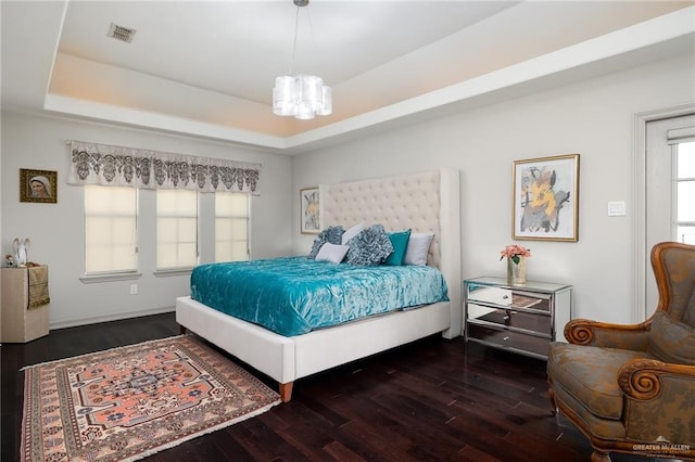 bedroom with a chandelier, dark hardwood / wood-style floors, and a tray ceiling