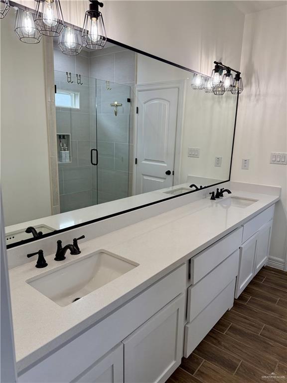 bathroom featuring a notable chandelier, wood tiled floor, a sink, and a shower stall