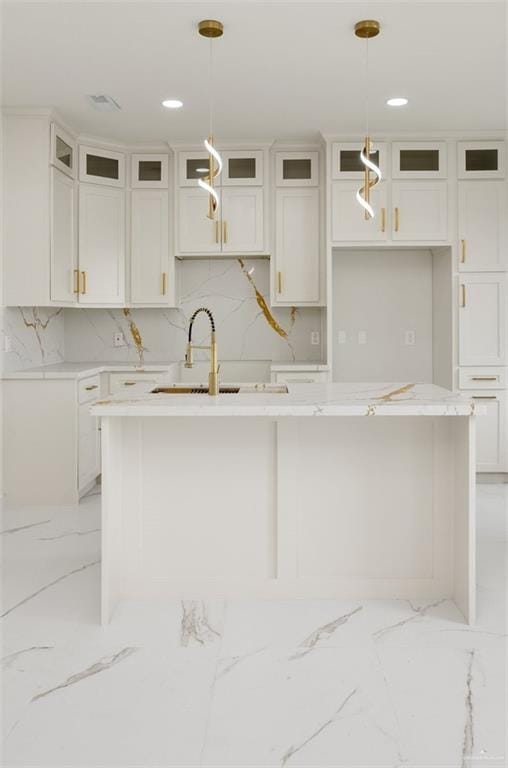 kitchen featuring marble finish floor, a kitchen island with sink, a sink, and white cabinetry