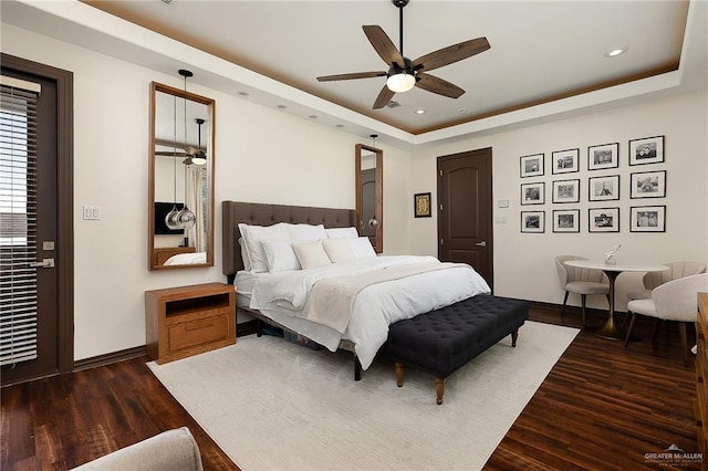 bedroom with dark hardwood / wood-style flooring, a tray ceiling, and ceiling fan