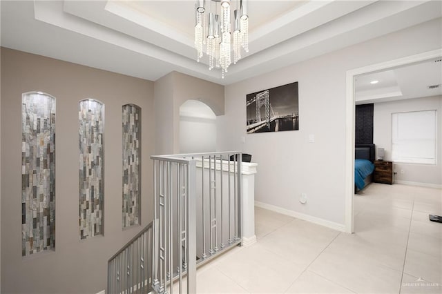 corridor featuring a tray ceiling, light tile patterned floors, arched walkways, and baseboards