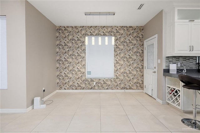 unfurnished dining area featuring an accent wall, light tile patterned flooring, baseboards, and visible vents