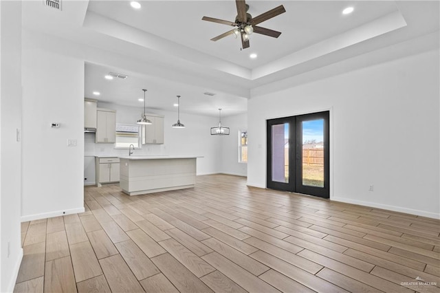 unfurnished living room with sink, light hardwood / wood-style flooring, ceiling fan, a raised ceiling, and french doors