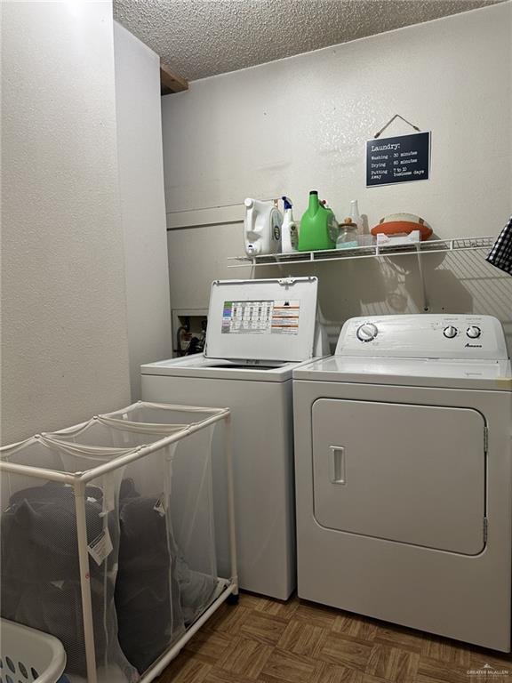 clothes washing area with washer and dryer, dark parquet flooring, and a textured ceiling