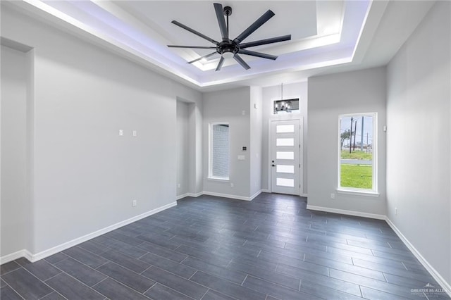 interior space featuring a raised ceiling, ceiling fan with notable chandelier, and dark hardwood / wood-style floors