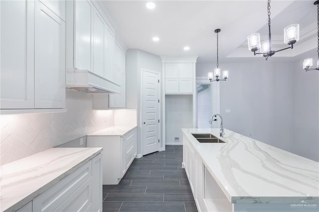 kitchen featuring white cabinets, sink, hanging light fixtures, light stone counters, and a chandelier